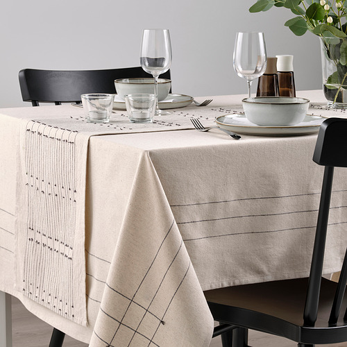 Mesa de comedor con corredor beige, patrones sutiles, borlas, sillas negras, cristalería, platos de cerámica para una comida acogedora.