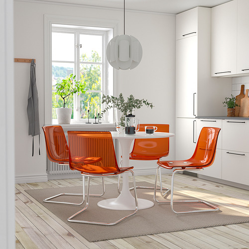 Cocina moderna con mesa DOCKSTA blanca, sillas naranjas, gran ventanal y luz colgante.