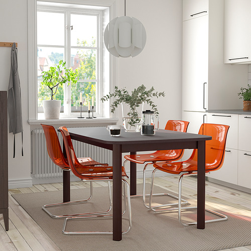 Mesa de comedor extensible STRANDTORP de color marrón oscuro con sillas naranjas. Diseño moderno y minimalista, encaja perfectamente debajo de la ventana, creando una acogedora zona de comedor.