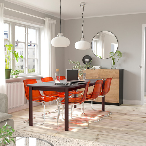 Comedor luminoso con modernas sillas naranjas, mesa extensible y gran ventanal, con un diseño elegante y minimalista.