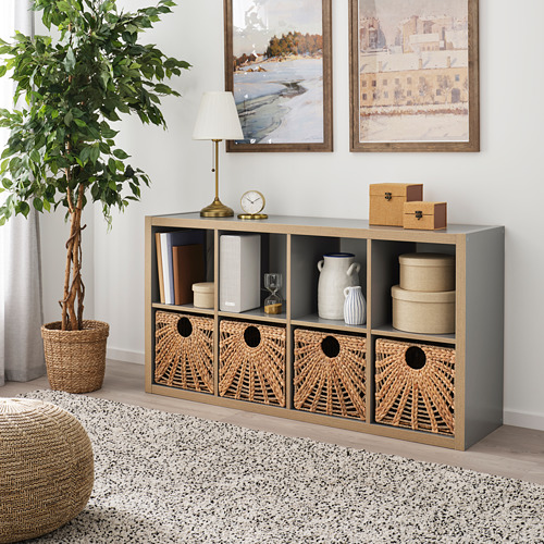 Sala de estar con cesta LUSTIGKURRE en estantería kallax, lámpara, reloj, libros, jarrones. Decoración acogedora y neutra.
