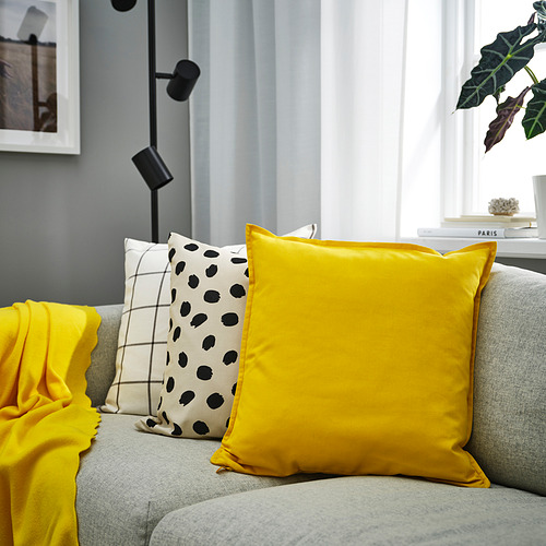 Sala de estar con sofá gris, gran almohada amarilla GURLI, además de otras más pequeñas a cuadros y puntos negros. Decoración luminosa y moderna.