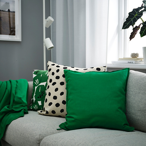 Acogedora sala de estar con sofá gris, cojines verdes, estantería para plantas y gran ventanal.