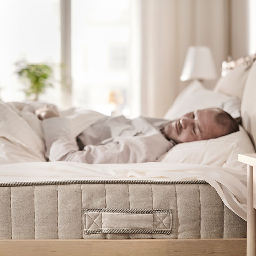 Una persona durmiendo plácidamente en un colchón VATNESTRÖM beige en un acogedor dormitorio con decoración de colores claros.