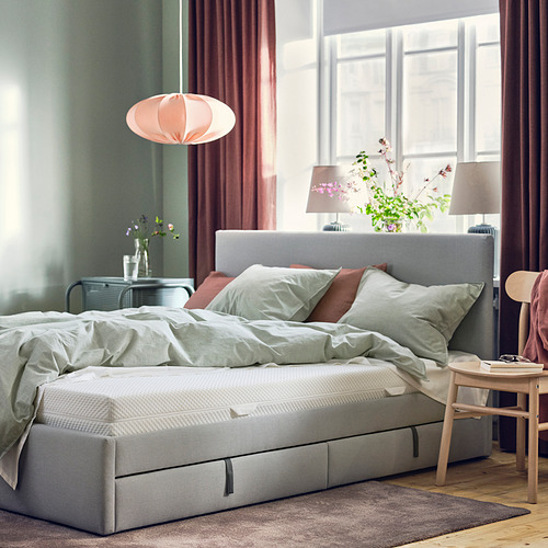 Acogedor dormitorio con cama gris, manta verde, lámparas rosas, cortinas rojas y flores.