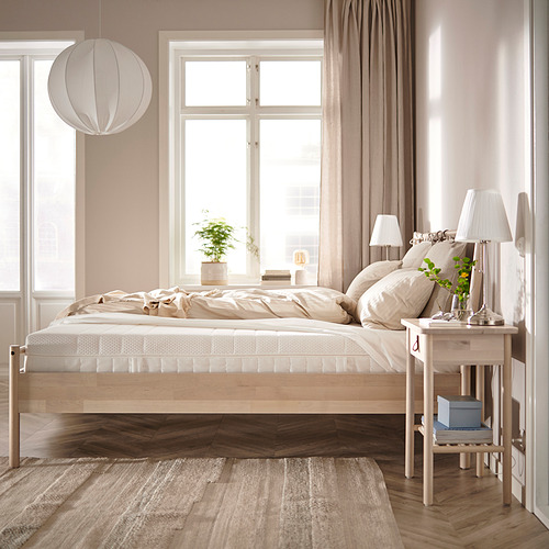 Dormitorio minimalista: cama de madera clara, ropa de cama neutra, grandes ventanales, lámpara colgante, mesita de noche con lámpara, planta.