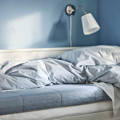 Un acogedor colchón de espuma azul en una habitación azul serena con una lámpara blanca, que muestra su diseño firme y cómodo.