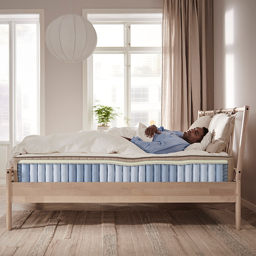 El hombre duerme en un colchón azul, firme, de muelles ensacados sobre una cama de madera, decoración natural.