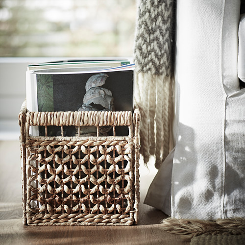 Cesta de mimbre con libros en el asiento, textiles suaves al lado, decoración natural y terrosa.