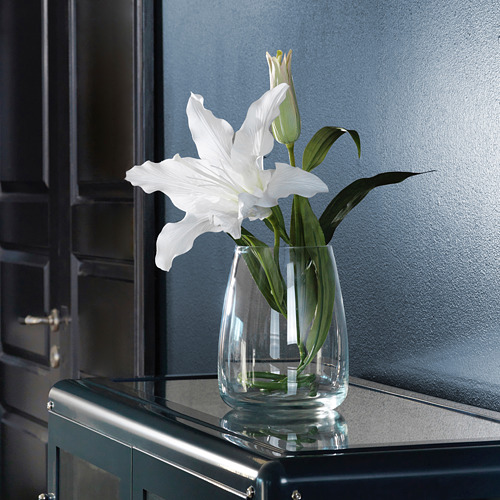 Jarrón de vidrio transparente con flor blanca sobre una superficie oscura.