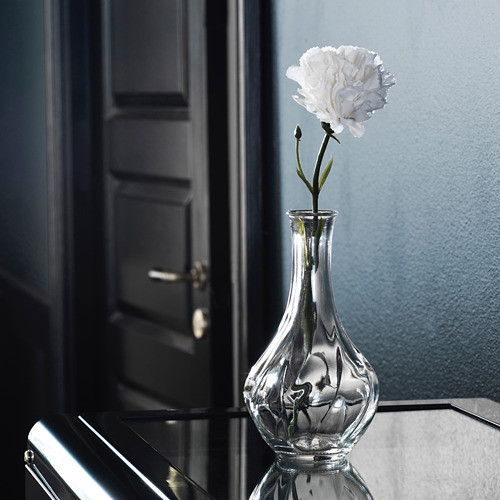 Jarrón de vidrio transparente con una sola flor blanca, diseño elegante, superficie reflectante, estilo elegante y minimalista.