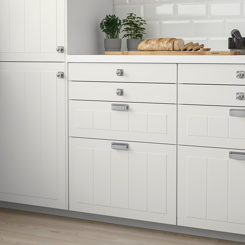 Modernos gabinetes de cocina blancos con manijas plateadas, piso de madera, plantas y pan. Diseño elegante y limpio.