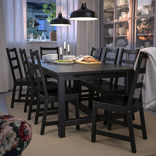 Juego de comedor con mesa y sillas NORDVIKEN negras, tres colgantes, platos, cubiertos y cocina al fondo.
