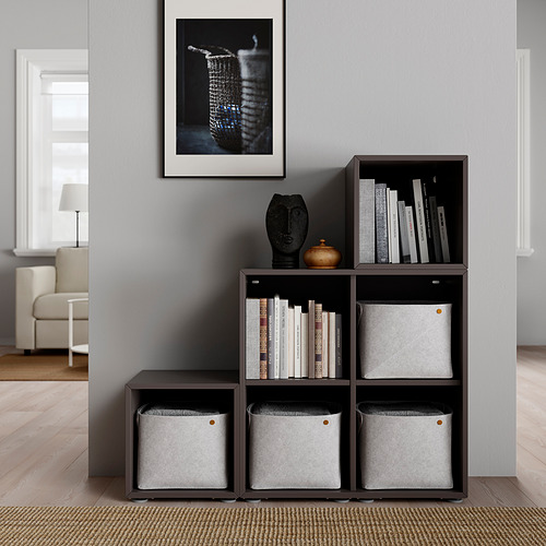 Estantería modular de color marrón oscuro con cubos de tela y libros, decorada, contra una pared gris con un cuadro enmarcado.