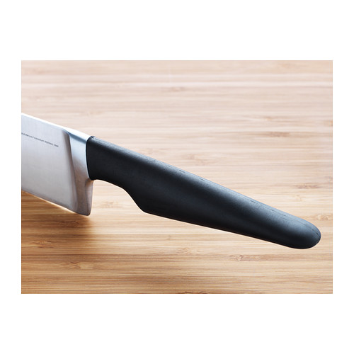 Un primer plano de un cuchillo de chef sobre una superficie de madera, con un mango negro y una hoja afilada de acero inoxidable.