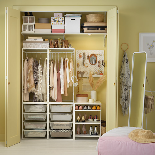 Armario organizado con almacenamiento JONAXEL blanco, perchas de ropa, estantes, y artículos de decoración; paredes amarillas.