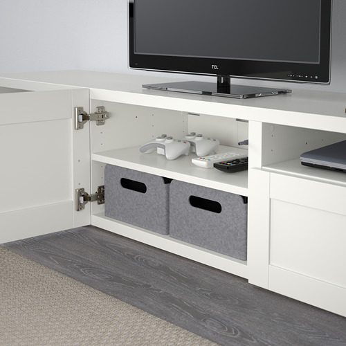 Mueble de TV BESTÅ blanco con bisagras de cierre suave, que sostiene un televisor, mandos de juegos y compartimentos de almacenamiento.