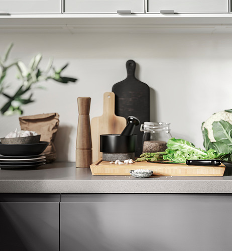 Una encimera de cocina con herramientas: mortero negro, mortero de madera, cuchillo, verduras, cuencos y platos.