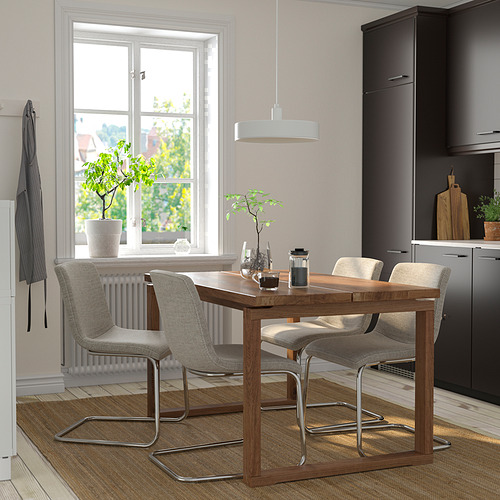 Comedor moderno con sillas beige LUSTEBO alrededor de una mesa de madera, debajo de una lámpara colgante, cerca de la ventana y la cocina.