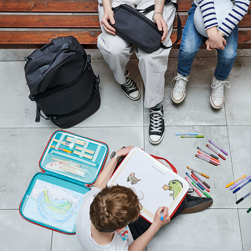 Niños en el banco, un dibujo con estuche de arte MÅLA abierto. Suministros coloridos y obras de arte en el suelo, una gran mochila al lado.