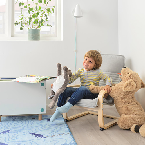Niño sentado en un mini sillón POÄNG con un peluche, junto a una mesa con libros en una habitación acogedora.