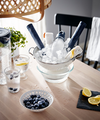 Mesa con arándanos, rodajas de limón, enfriador de bebidas lleno de hielo y vasos. Comedor moderno de madera.