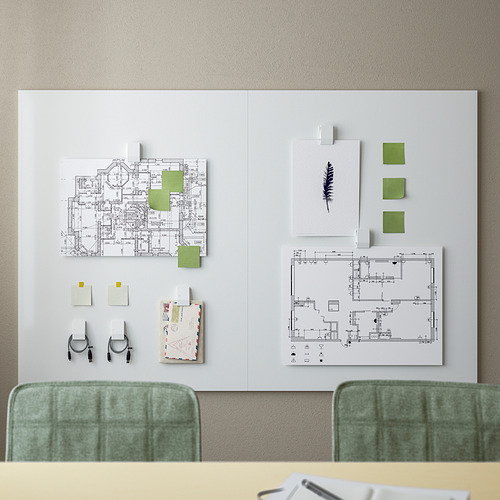 Una pizarra blanca con un marco verde y sillas verdes. El tablero muestra planos arquitectónicos y notas adhesivas de colores, destacando la configuración de un espacio de trabajo.
