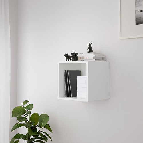 Cubo de almacenamiento blanco montado en la pared que contiene libros y figuras decorativas negras, con una planta en maceta debajo.