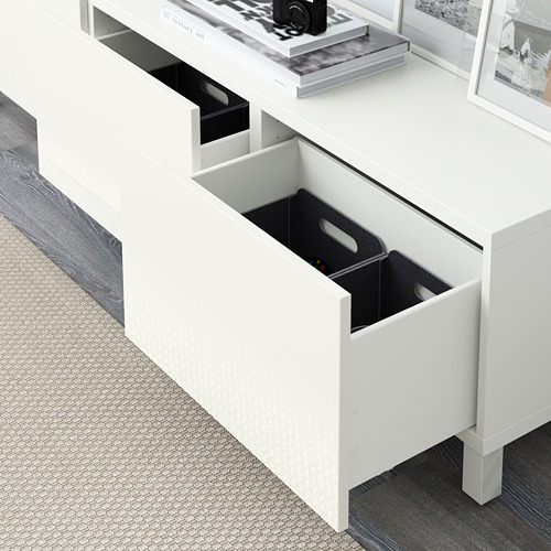 Cómoda blanca BESTÅ con cajón abierto de par en par que revela organizadores interiores negros sobre suelo de madera.