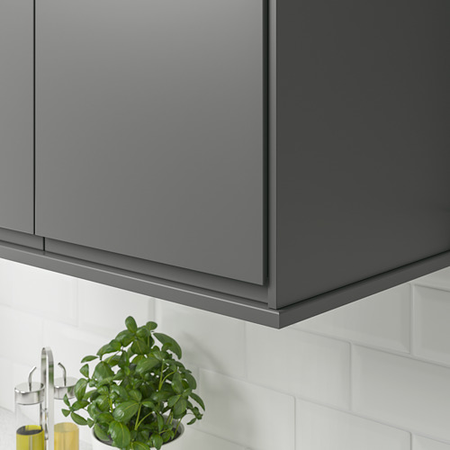 Gabinetes de cocina grises con un protector contra salpicaduras de azulejos blancos. Debajo de los armarios, hay una planta y botellas de aceite.