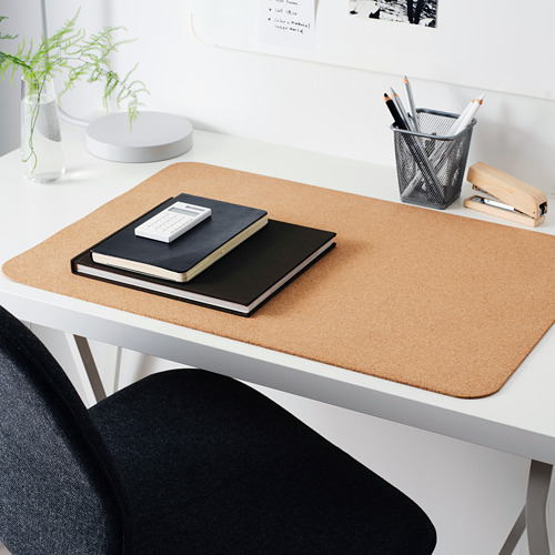 Almohadilla de escritorio de corcho beige sobre escritorio blanco, con cuadernos, helecho, portalápices y grapadora.