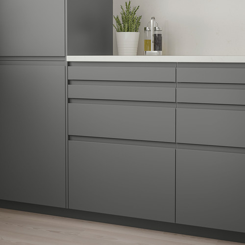 Los modernos muebles de cocina grises con elegantes cajones oscuros presentan un diseño minimalista que se combina a la perfección. Las plantas y los tarros de aceite encimeran blancos compactos.