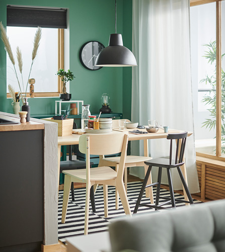 Comedor moderno con paredes verdes, plafón negro, mesa de madera, cuatro sillas de madera clara, alfombra a rayas y gran ventanal con cortinas blancas.