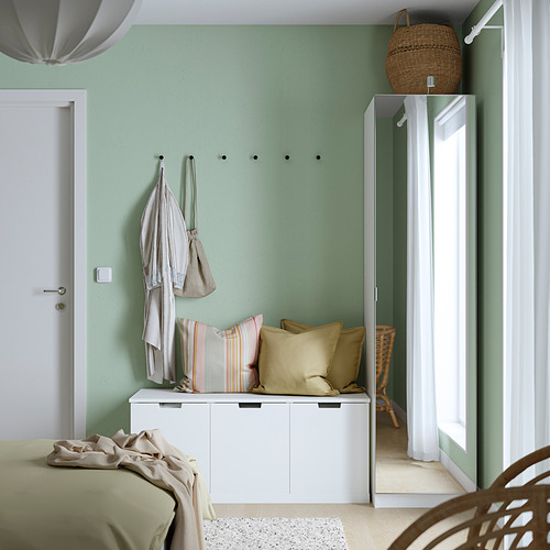 Dormitorio moderno con armario PAX blanco, cortinas transparentes, chaquetas ligeras, cesta y cama con manta verde.
