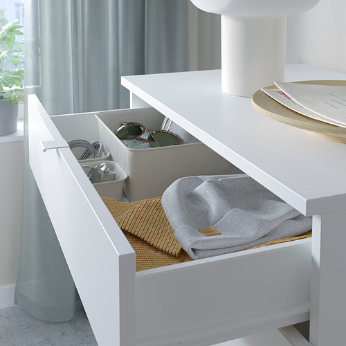 Cajonera blanca con compartimentos grises y paño gris doblado en el interior, dispuesta sobre una mesa.