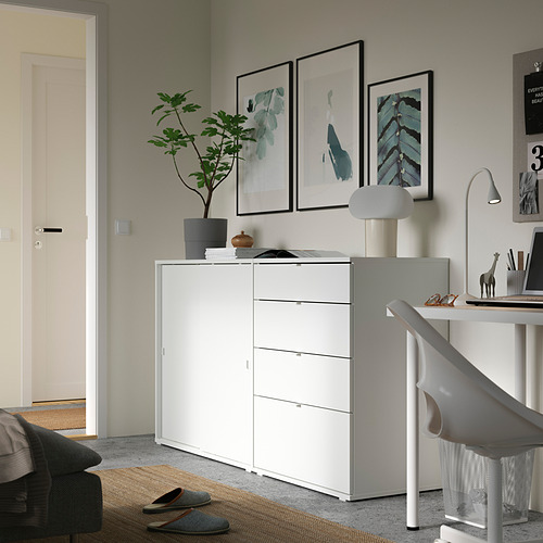Moderna oficina en casa minimalista. Mueble de almacenaje blanco, silla gris, láminas artísticas, planta, lámpara.