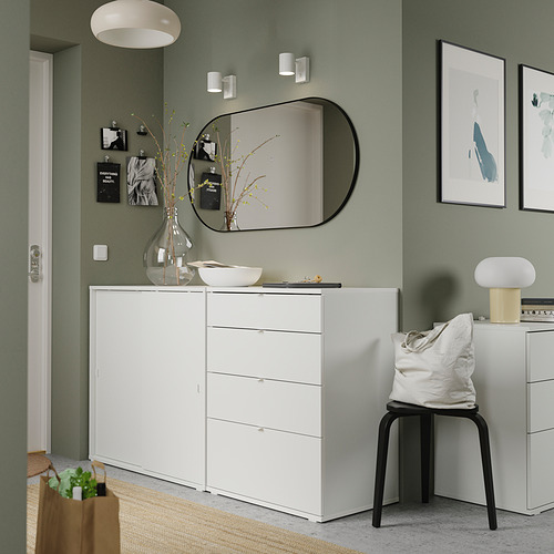 Moderna sala verde con muebles blancos que incluyen una cómoda, una silla y un taburete. Obras de arte, un espejo y artículos decorativos.