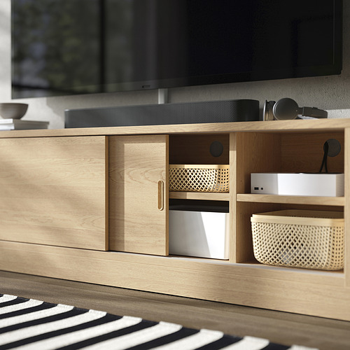 Mueble de TV de madera con puertas correderas, gestión de cables y estantes ajustables, que albergan dispositivos electrónicos y compartimentos de almacenamiento.