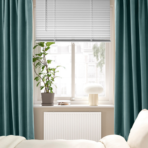 Ventana moderna con persianas blancas VECKLARFLY, cortinas turquesa, planta y lámpara en el alféizar, radiador blanco debajo.