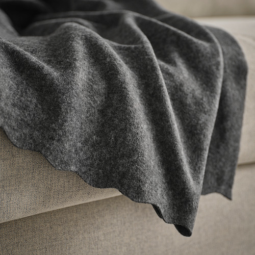 Una suave manta de vellón gris oscuro sobre un sofá o cama beige. La textura se ve acogedora y acogedora, ideal para brindar calidez.