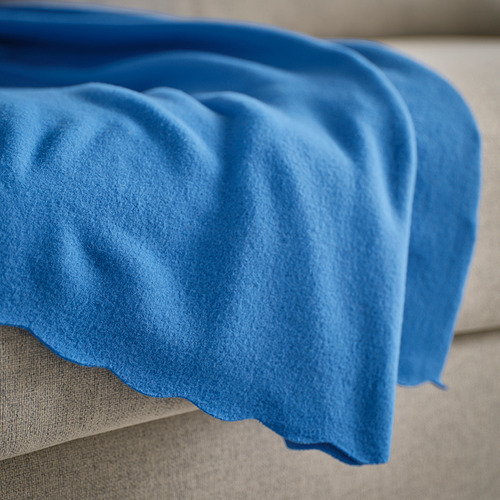 Manta de vellón azul brillante sobre un sofá beige, mostrando su textura suave.