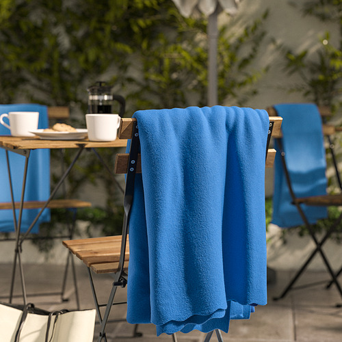 Manta de vellón azul cubierta en una silla cerca de la configuración de un café al aire libre con tazas y mesa.