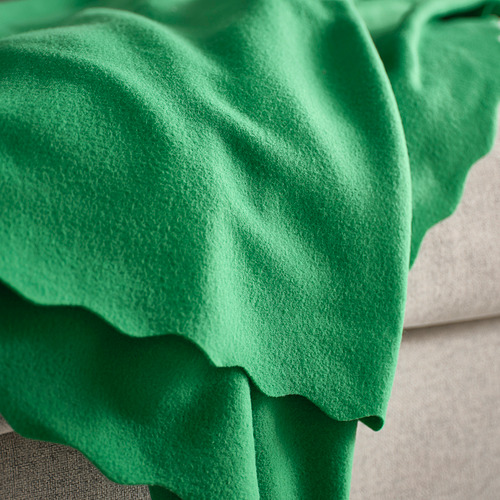 Manta polar verde, textura suave, drapeada sobre cojín.
