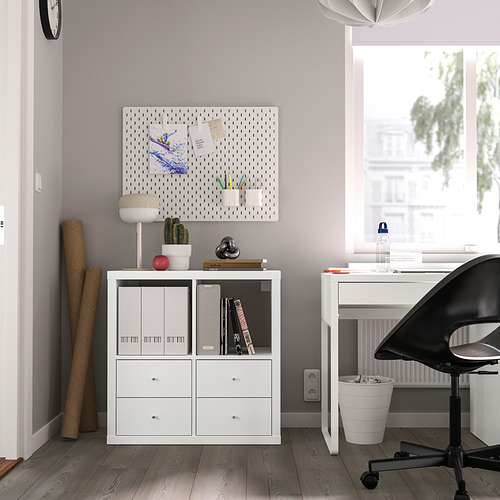 Oficina en casa minimalista con unidad KALLAX, notas, cactus, lámpara y arte de tablero perforado. Silla negra en el escritorio junto a la ventana.