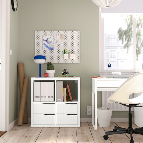 Estantería KALLAX con libros, planta, lámpara y notas. Escritorio blanco con computadora y silla cerca de la ventana.