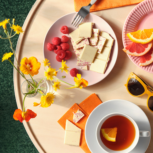 Plato con chocolate blanco, frambuesas y una taza de té. Flores y rodajas de cítricos cerca.