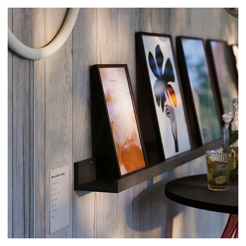 Estantería de pared con fotos enmarcadas, botella verde sobre mesa pequeña.