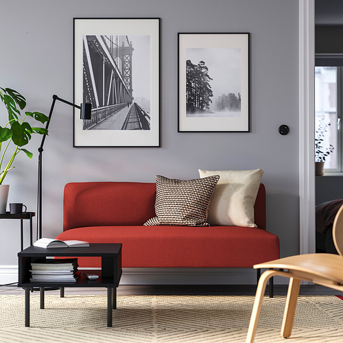 Moderno salón con sofá LILLEHEM rojo, almohadas, mesa de centro negra, planta, lámpara y fotos en pared gris.