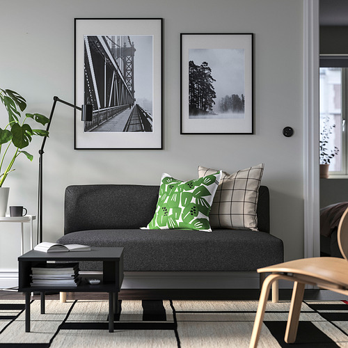 Salón moderno con sofá LILLEHEM gris, almohada verde, estampados en la pared, planta y mesa de centro.