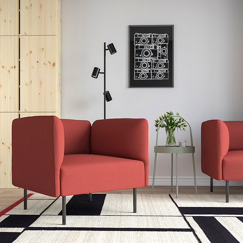 Habitación moderna con dos sillones LILLEHEM rojos, alfombra blanca y negra, mesita y arte de pared. Los sillones dominan el espacio, con iluminación natural.